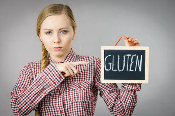 Young woman with braided hair holding small black board with gluten sign. Bakery and bread allergy problem.