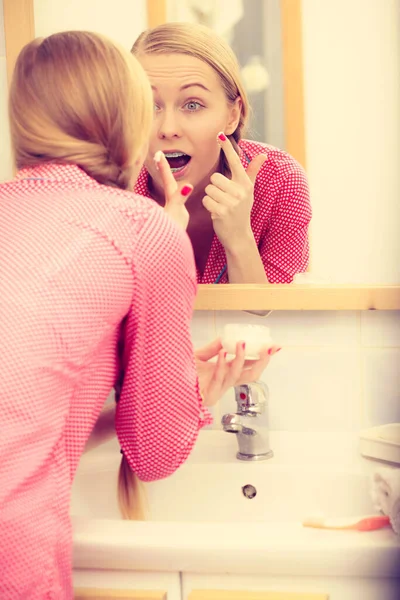 Genç Sarışın Kadın Yüzüne Nemlendirici Krem Sürüyor Banyo Aynasına Bakıyor — Stok fotoğraf