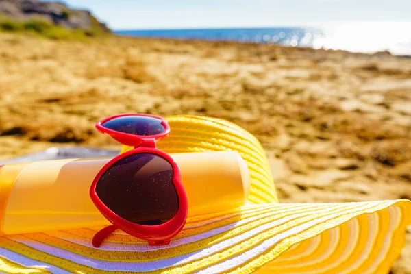 海岸沿いの太陽の保護アクセサリー 砂浜の赤いサングラス 黄色の麦藁帽子と日焼け止めクリームボトル 夏休み — ストック写真