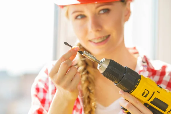 Young woman adjusting, changing her drill bit doing home renovation. Female construction worker having driller tool working on diy.