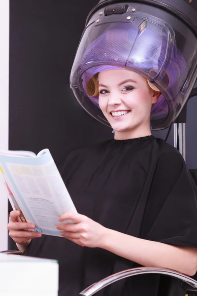 Girl relaxing reading magazine hairdryer by hairstylist in hair beauty salon Stock Image