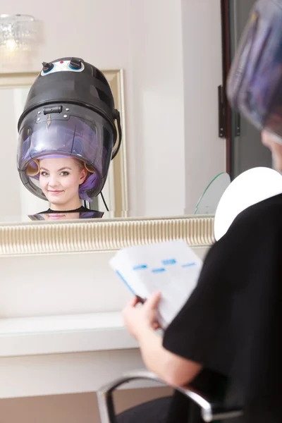 Femme client bigoudis dans les cheveux lit magazine coiffure salon de beauté. — Photo
