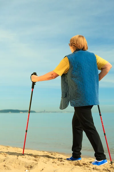 Active woman senior nordic walking on a beach. from behind — Stock Photo, Image