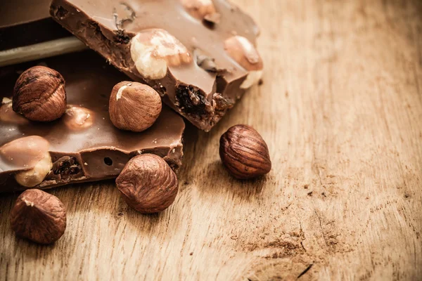 Milk chocolate and hazelnuts on wooden table — Stock Photo, Image