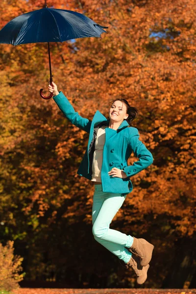 Sonbahar parkında mavi şemsiyeyle atlayan kız — Stok fotoğraf