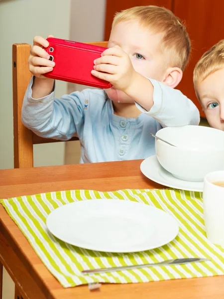 Chlapec slintání stravování snídaně, hraní s mobilním telefonem — Stock fotografie