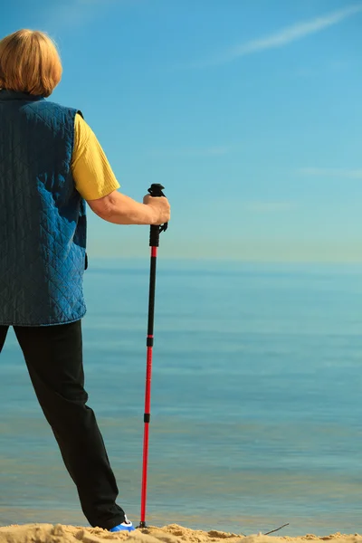 Aktive Seniorin beim Nordic Walking am Strand. von hinten — Stockfoto