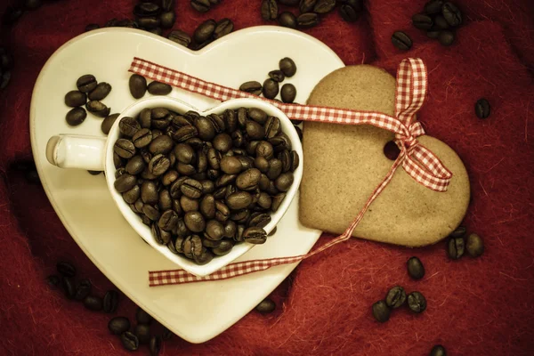 Coffee beans in heart shaped cup and dessert on red — Stock Photo, Image