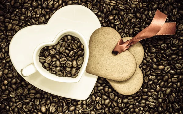 Heart shaped cup and cookie on coffee beans background — Stock Photo, Image