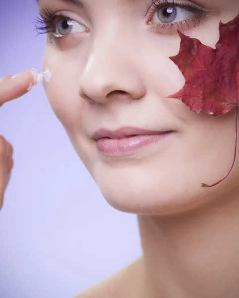 Huidverzorging. Gezicht van jonge vrouw meisje met rode esdoorn blad. — Stockfoto