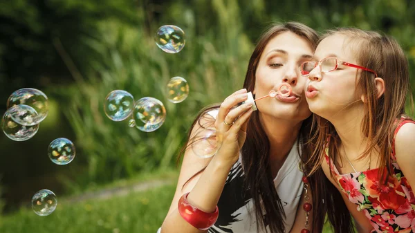 Mother and little girl blowing soap bubbles — Stock Photo, Image