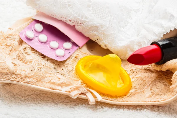 Таблетки, презерватив и помада на кружевном белье — стоковое фото