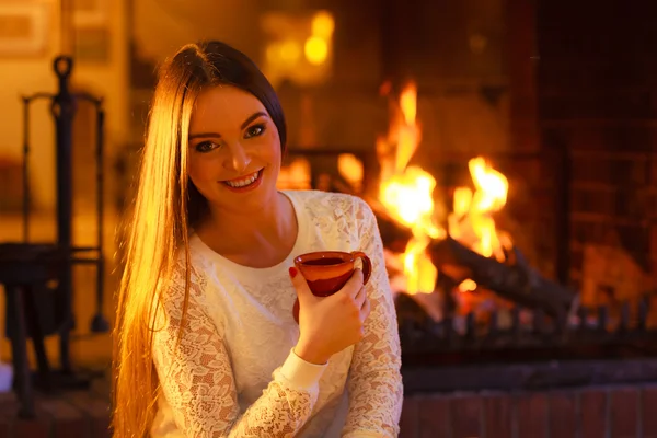 暖炉のそばでウォーミング アップの女の子を保持するマグカップ — ストック写真