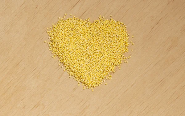 Heart shaped Millet groats on wooden surface. — Stock Photo, Image