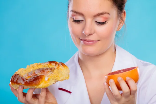 Nutricionista sosteniendo un pastel y fruta — Foto de Stock