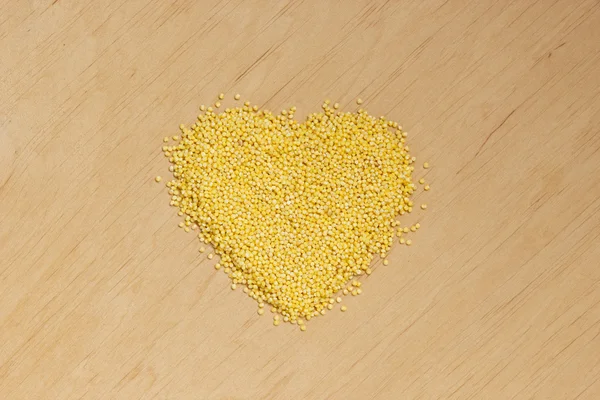 Heart shaped Millet groats on wooden surface. — Stock Photo, Image