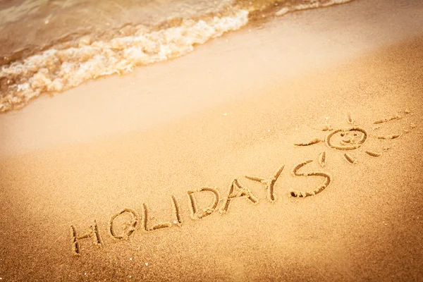 The word holidays written in the sand on a beach — Stock Photo, Image