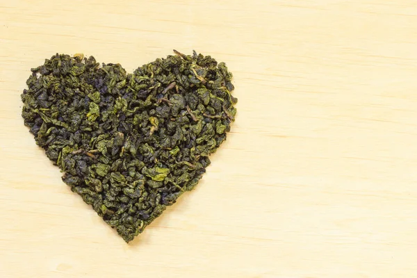 Kalp şeklinde ahşap yüzeyde yeşil çay yaprakları — Stok fotoğraf