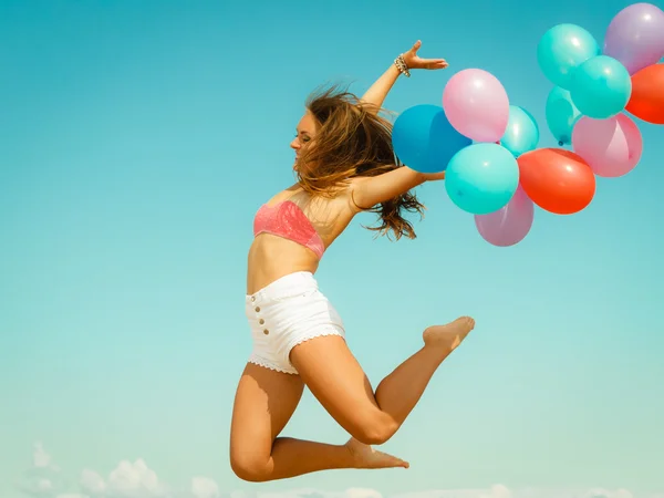 Mädchen springt mit bunten Luftballons am Strand — Stockfoto