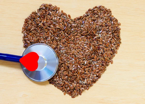 Сырые семена льна в форме сердца и стетоскопа — стоковое фото