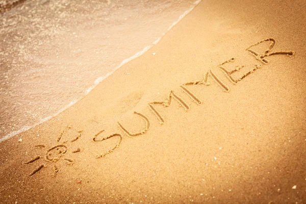 Het woord zomer geschreven in het zand op een strand — Stockfoto