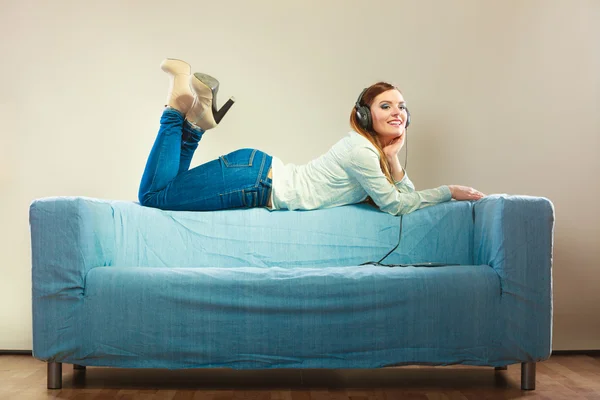 Женщина в наушниках лежит на диване — стоковое фото