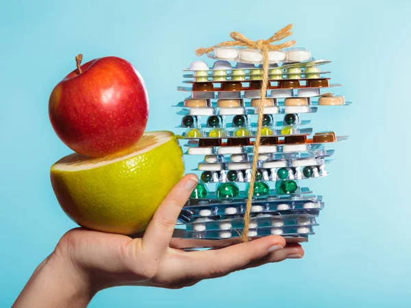 Human hand holding stack of pills and fruits on blue. — Stock Photo, Image
