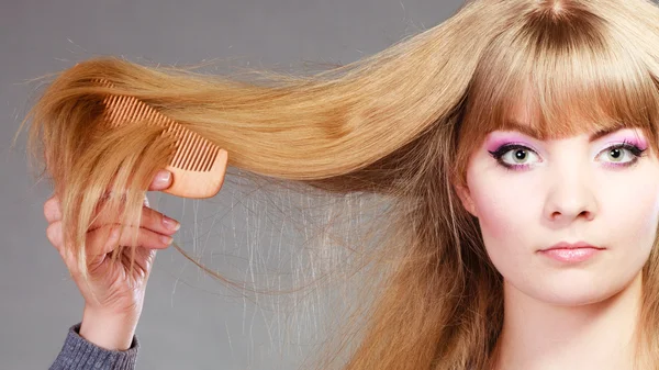 Blonde woman combing hair.