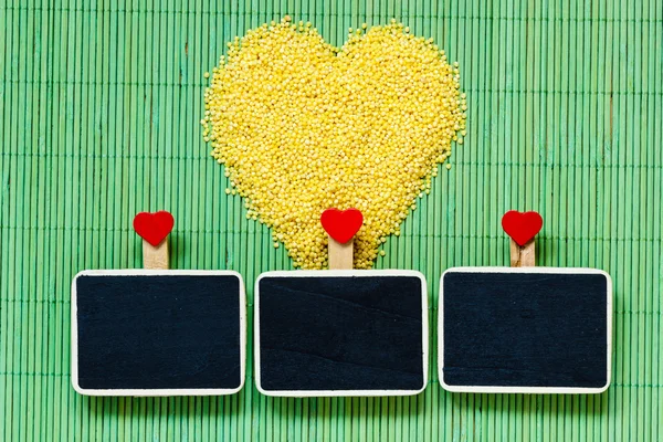 Millet groats heart shaped on green mat surface. — Stock Photo, Image