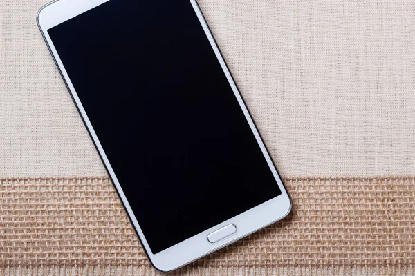 Smartphone blanco moderno con pantalla en blanco se encuentra en textil. — Foto de Stock