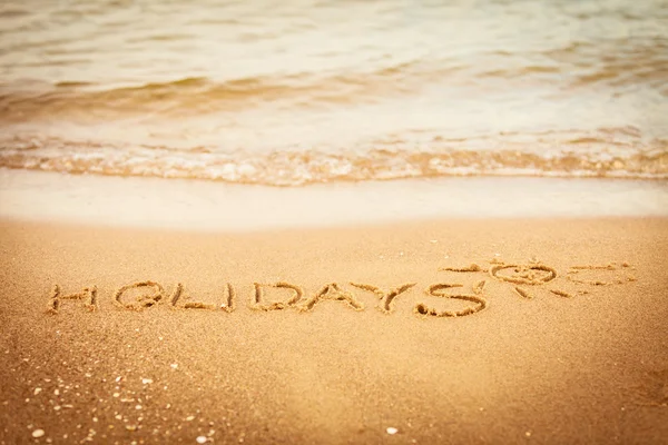 De vakantie van de woord geschreven in het zand op een strand — Stockfoto