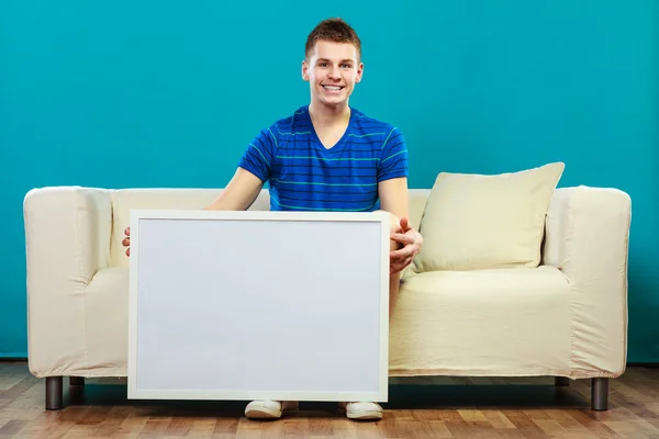 Man on sofa holding blank presentation board — Stock Photo, Image