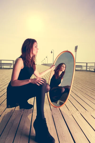Thoughtful woman looks at reflection in mirror — Stock Photo, Image