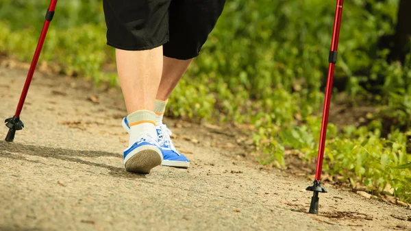 Actieve senior benen in sneakers nordic-walking in een park. — Stockfoto