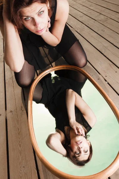 Thoughtful woman looks at reflection in mirror — Stock Photo, Image