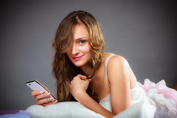 Mujer en la cama sosteniendo teléfono móvil. — Foto de Stock