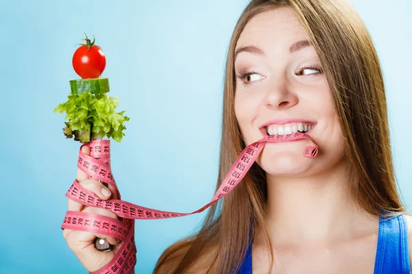 Woman biting measuring tape with vegetables. — Stock Photo, Image