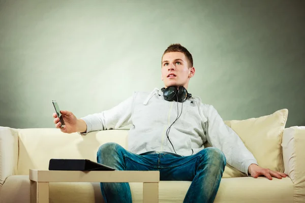 Uomo su divano con cuffie smartphone e tablet — Foto Stock
