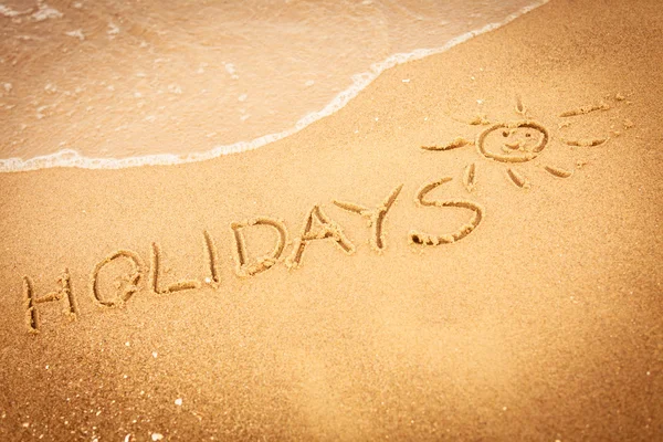 La palabra vacaciones escrita en la arena en una playa — Foto de Stock