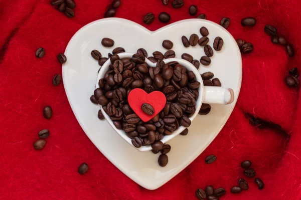 Heart shaped cup with coffee beans on red — Stock Photo, Image