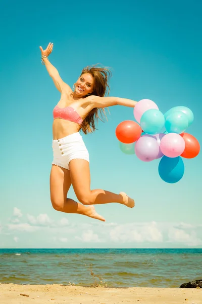 Meisje springen met kleurrijke ballonnen op het strand — Stockfoto