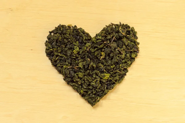 Green tea leaves heart shaped on wooden surface — Stock Photo, Image