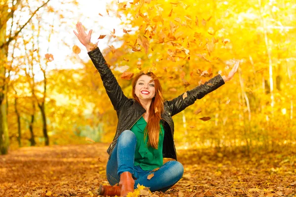 Девушка отдыхает в осеннем парке, подбрасывая листья в воздух.. — стоковое фото