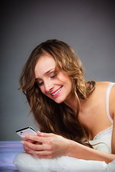 Mujer en la cama sosteniendo teléfono móvil. — Foto de Stock