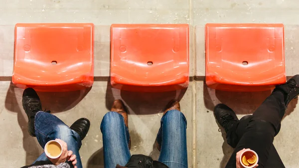 Row of plastic chairs and legs in football stadium.