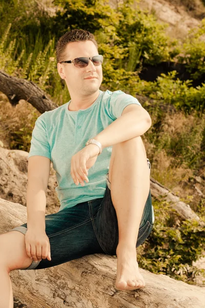 Fashion portrait handsome man sitting on tree — Stock Photo, Image