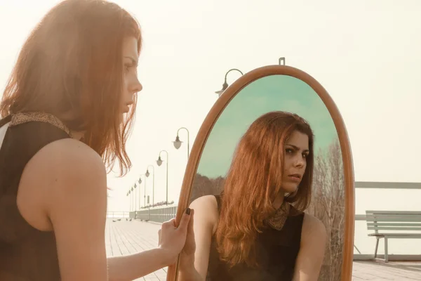 Thoughtful woman looks at reflection in mirror — Stock Photo, Image