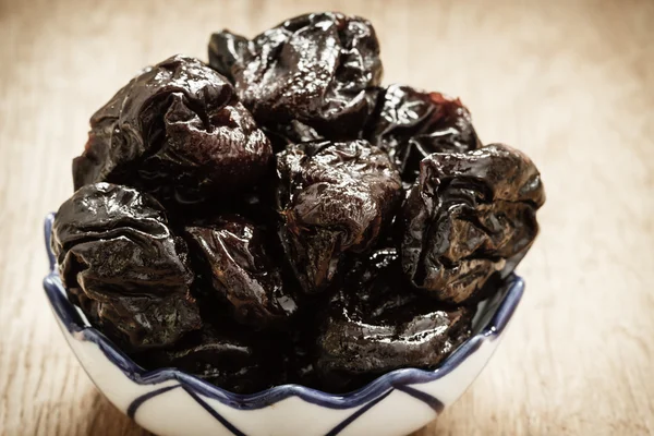 Dried plums prunes in bowl on wooden table — Stock Photo, Image