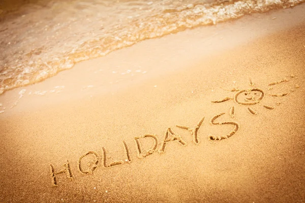 The word holidays written in the sand on a beach — Stock Photo, Image