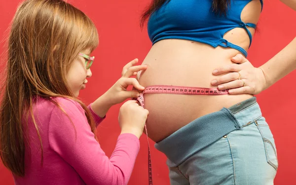 Liten flicka mätning av mammas mage — Stockfoto